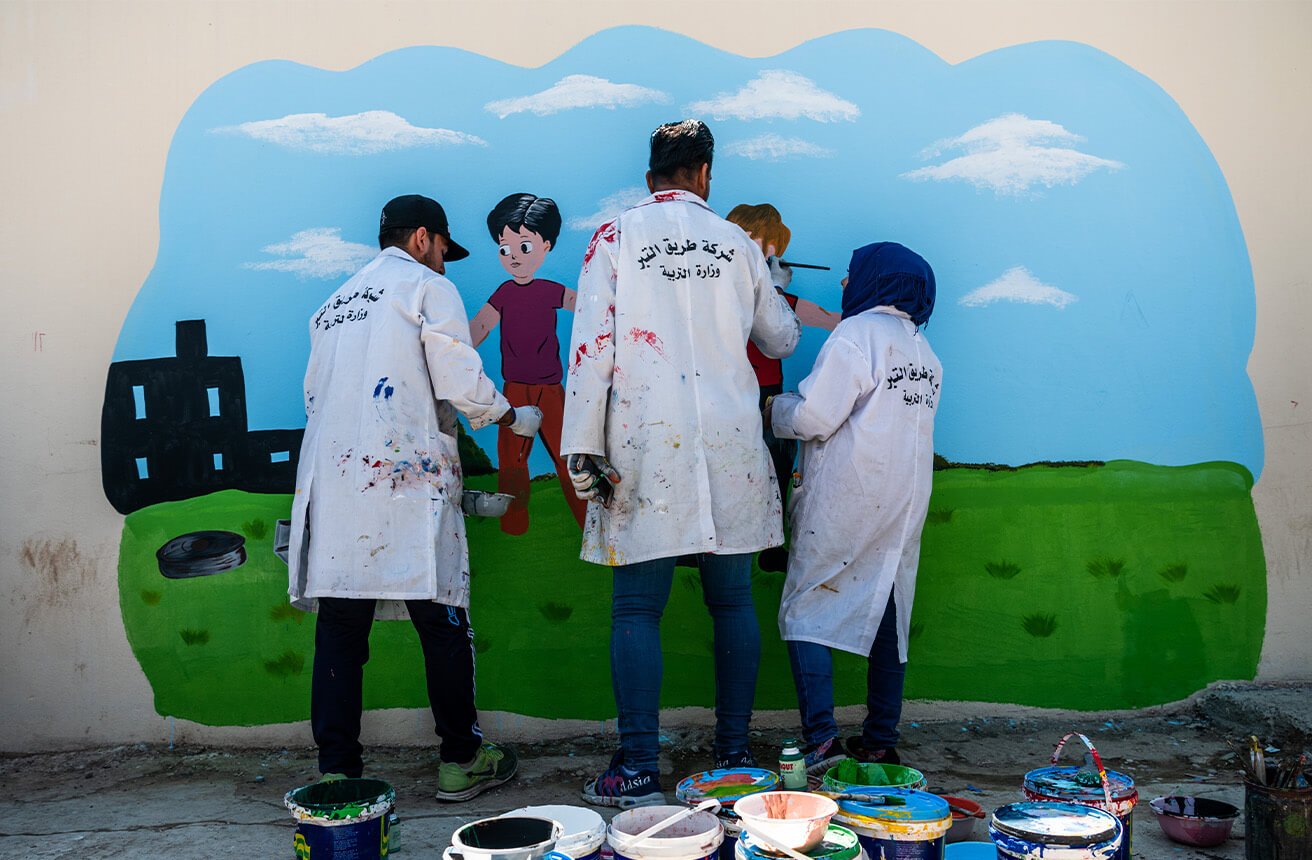 Tres personas pintando murales coloridos en una pared de la escuela primaria Al Mansour en Irak.